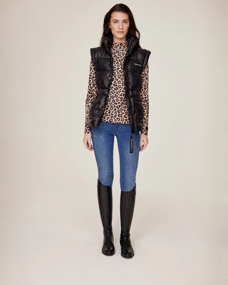 Full body front view of the unzipped black puffer vest showcasing the layered look with denim breeches.