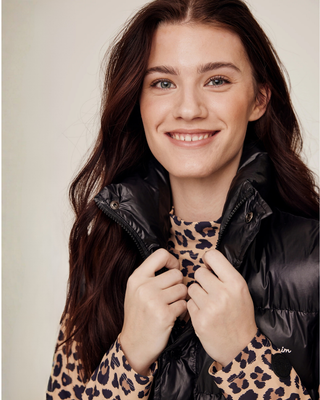 Portrait of the model holding the high collar of the black riding vest, showing the premium semi-glossy texture.