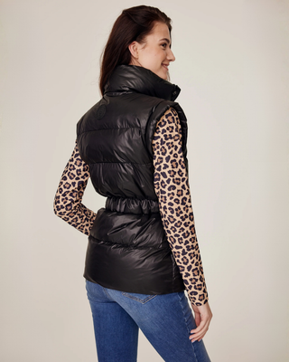 Side profile shot of the model wearing the semi-glossy black puffer vest and leopard print riding top.