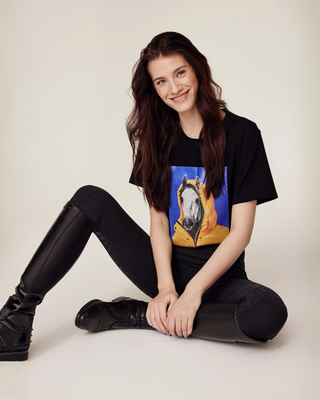 Relaxed sitting model wearing black riding tights and the signature black t-shirt with a white horsie print.