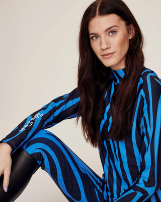 Sitting model posing in the complete blue zebra riding set, showcasing the four-way stretch performance material.