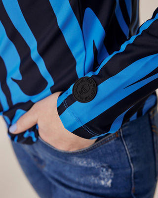 Close-up of the sleeve featuring the Riders Denim logo on blue zebra fabric, with the model's hand in her denim breeches pocket.