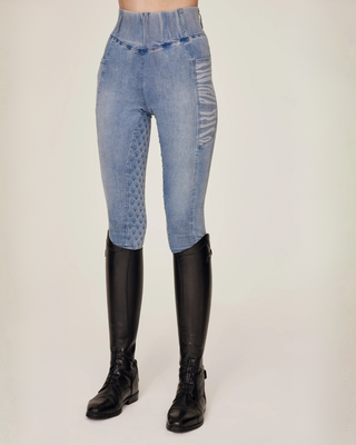 Angled front view of the light blue denim riding breeches styled with professional black riding boots.