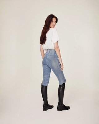 Full body shot of the model in light blue jeans breeches and leo top, looking to the side in a stable setting.