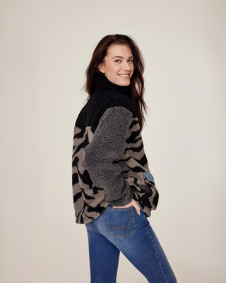 Angled back view of the lilac and zebra teddy jacket with the model's hand in the back pocket of her denim riding breeches. 