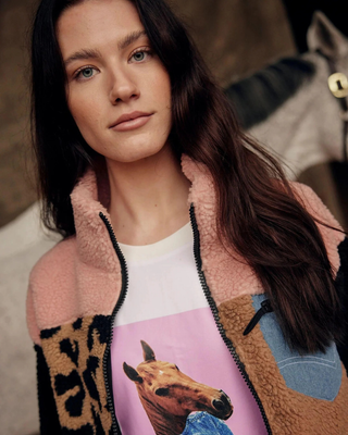 ortrait of a model in the Pink and Leo teddy jacket and white horse t-shirt with a grey horse in the background.