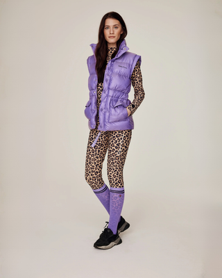 Full body shot of a model wearing a complete leopard print riding set, lilac puffer vest, and matching lilac riding socks.